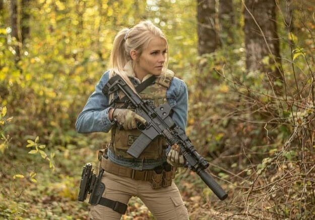 A woman holding an ar-1 5 rifle in the woods.